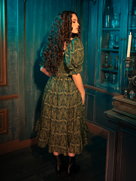 Embrace the dark allure of the CRIMSON PEAK™ Allerdale Moth Wallpaper Babydoll Dress. The olive backdrop, rich and earthy, sets the stage for a dance of moths — creatures of the night drawn to the unseen and the unknown. This dress embodies the delicate balance between darkness and light, offering a unique statement piece for those who walk the path less traveled.