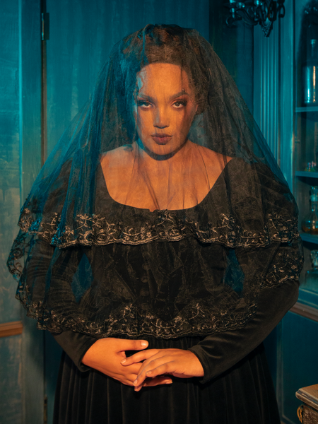 Capturing an air of contemplation, a Gothic female model showcases the Black Veil with Embroidered Lace Trim from the gothic clothing brand La Femme en Noir, striking pensive poses that infuse a sense of mystery into the ensemble.