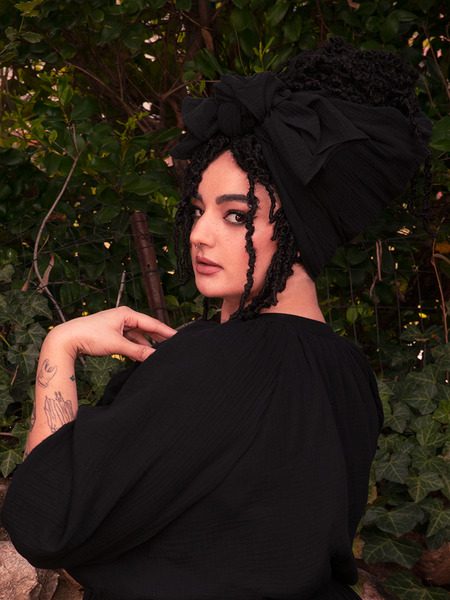 Prepare to be entranced by the mysterious allure of the model, veiled in the enigmatic Coven Head Wrap in Black, an embodiment of gothic mystique from the revered retro clothing brand, La Femme en Noir Clothing.