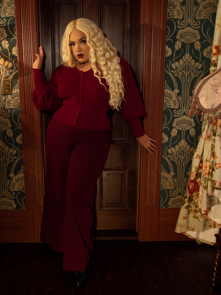 A cascade of oxblood crepe trails every step like spilled wine, echoing the drama of a gothic opera's final note.