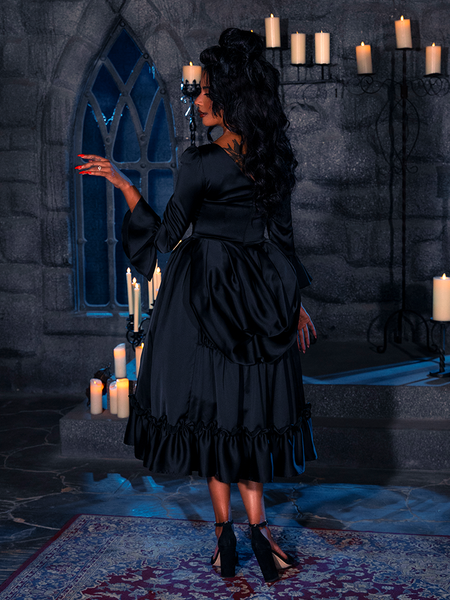 Cloistered in a candlelit chamber, the captivating siren exhibits the Obsidian Orchid Silk Bustier Robe, a creation of the illustrious gothic atelier, La Femme en Noir.