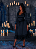 Veiled by the spectral radiance of candle flames, the captivating muse showcases the Shadowed Elegance Satin Bustle Dress in Black, a creation from the depths of the gothic design coven known as La Femme en Noir.