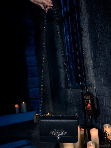 Bathed in the eerie radiance of candle flames, the Gargoyle Sculpture Quilted Crossbody Bag in Black, a product of gothic clothing brand La Femme en Noir's BRAM STOKER'S DRACULA line, makes its presence known.