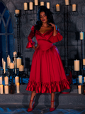 In a dungeon room bathed in the warm glow of candles, a beautiful model showcases the BRAM STOKER'S DRACULA Mina Satin Bustle Dress in Blood Red with grace.