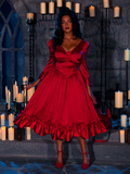 In a dungeon room softly illuminated by candles, a beautiful model showcases the BRAM STOKER'S DRACULA Mina Satin Bustle Dress in Blood Red with grace.