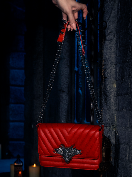 Embraced by the soft, eerie glow of candlelight, the BRAM STOKER'S DRACULA Gargoyle Sculpture Quilted Crossbody Bag in Blood Red is showcased, a masterpiece by the gothic artisans at La Femme en Noir.