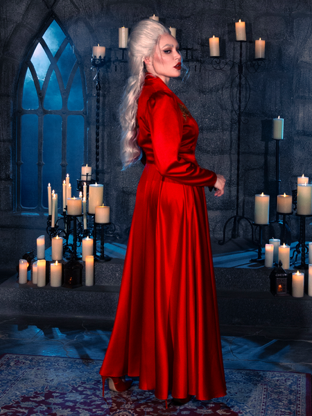 In a candlelit dungeon, a female model epitomizes gothic style, donning the BRAM STOKER'S DRACULA Embroidered Order of the Dragon Wrap Dress in Scarlet Red, a remarkable creation from the goth clothing brand La Femme en Noir.