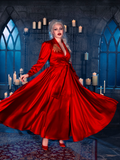 Dressed in the BRAM STOKER'S DRACULA Embroidered Order of the Dragon Wrap Dress in Scarlet Red, a female model captures the essence of gothic clothing within the atmospheric setting of a candlelit dungeon, courtesy of La Femme en Noir's unique designs.