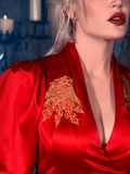 In a dimly lit dungeon, a female model embodies her chic style with the BRAM STOKER'S DRACULA Embroidered Order of the Dragon Wrap Dress in Scarlet Red, a captivating garment from the gothic fashion collection of La Femme en Noir.