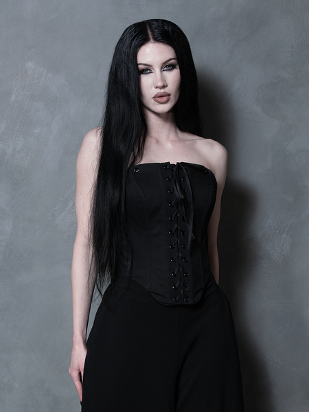 A female model evokes a sense of tragic romance and dark elegance, wearing a luxurious black sateen corset.