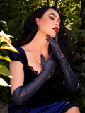Micheline Pitt exudes allure as she poses seductively in a concealed garden, donning the Navy Faux Leather Opera Gloves from the gothic clothing brand La Femme en Noir.