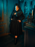 In the folds of this dress, gothic romance is reborn. The black fabric and accompanying capelet are the setting for a tale of love eternal, a romance that whispers through the ages, as timeless as the design itself.
