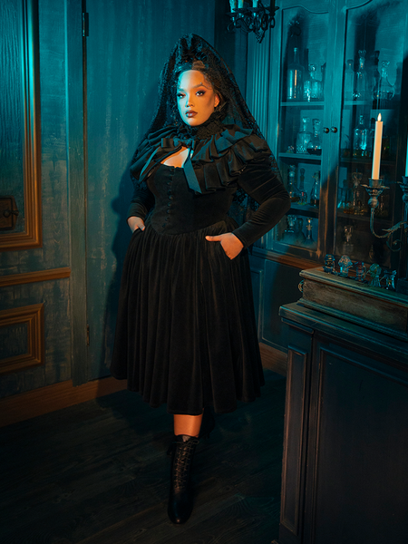  In the folds of this dress, gothic romance is reborn. The black fabric and accompanying capelet are the setting for a tale of love eternal, a romance that whispers through the ages, as timeless as the design itself.