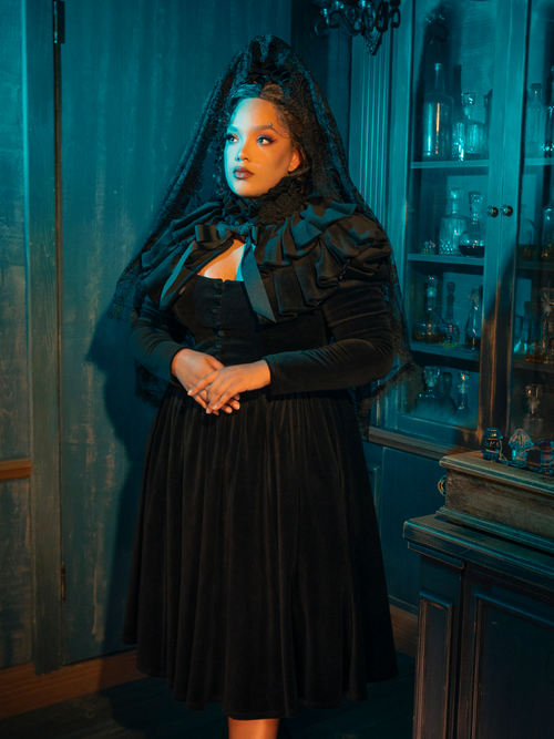 The Haunted Beauty Victorian Mourning Dress with Capelet in Black wraps you in the velvet night. Its capelet, like the wings of a raven, whispers tales of love lost and the solemn beauty found in grief. This ensemble is a tribute to the art of mourning, a wearable elegy that speaks to the soul.