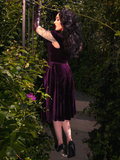 Amidst the clandestine beauty of a garden, Micheline Pitt poses seductively in the Plum Baudelaire Swing Dress from La Femme en Noir.