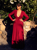 Ashleeta stands in a garden with her face shadowed by a tree while modeling the Art Deco gown in crimson.