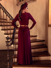 A back view of Aliza, standing on the staircase of a palatial home, models the Art Deco ruched gown in crimson from La Femme En Noir.