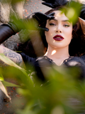 Close up of Micheline Pitt laying down on a stone bench while wearing the Baudelaire Wiggle Dress in Black.
