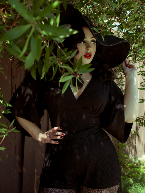 Rachel stands under a tree looking to the side of the camera while modeling the Bauhaus top in black from La Femme En Noir.