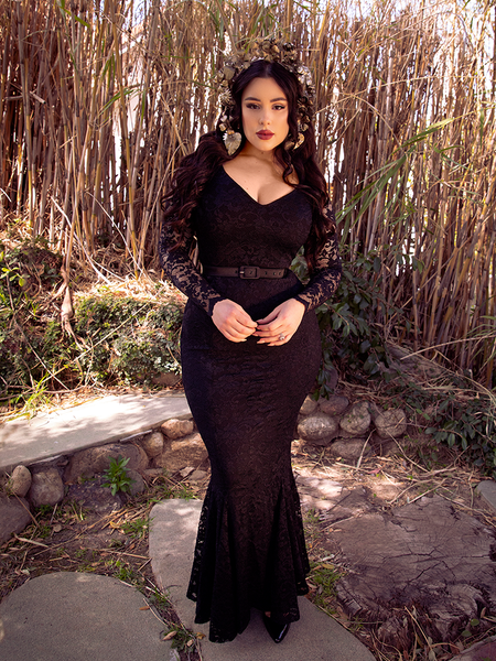 Gently lit by light, Rachel Sedory wears the Black Marilyn Lace Gown in Black while standing in a bamboo garden.