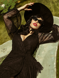 Micheline Pitt laying down and sunbathing while modeling the Black Widow Wrap Gown in Black Lace.
