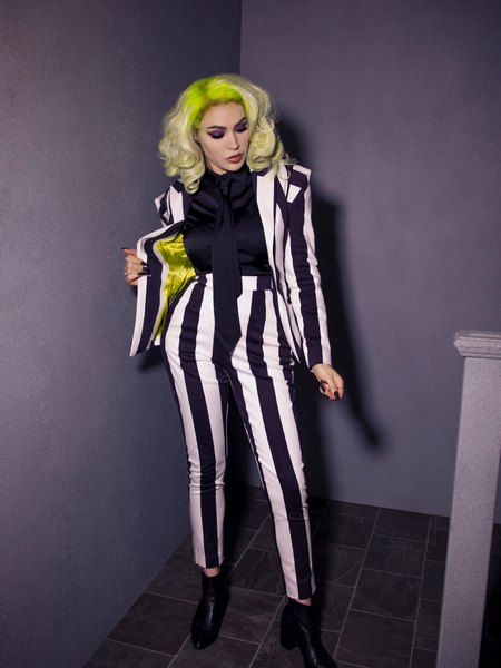 Full length shot of Micheline Pitt wearing a black and white striped jacket and pant combo with the Bowie Blouse w/Matching Tie in Black Charmeuse on underneath.
