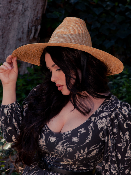 La Femme en Noir's Cottage Witch Hat in Natural adds a unique and captivating twist to the dark haired female model's stunning gothic clothing outfit.