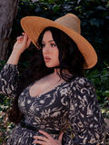 The gothic clothing outfit worn by the dark haired female model is beautifully accentuated by La Femme en Noir's Cottage Witch Hat in Natural, making her look stunning.