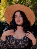 The dark haired female model looks hauntingly beautiful in her gothic clothing outfit, which is complemented perfectly by La Femme en Noir's Cottage Witch Hat in Natural.