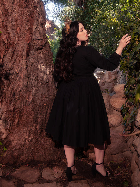 Surrounded by the enchanting allure of a forest, a gorgeous brunette model graces the scene, wearing the elegant Dark Forest Dress in Black, a remarkable creation by the gothic clothing brand, La Femme en Noir.