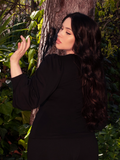 Against the backdrop of a mystical wooded forest area, a brunette model showcases the Black Dark Forest Blouse in all its glory. Step into the world of La Femme en Noir for this exquisite piece.