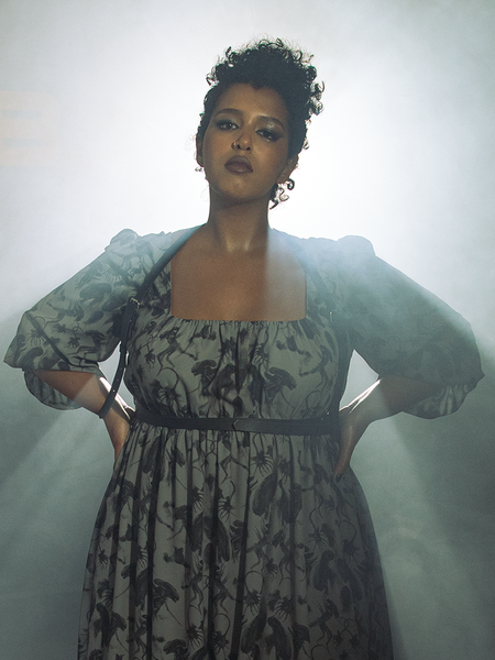 Model backlit by bright white light wearing the Body Strappy Harness in Black Faux Leather.