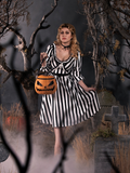 Linda, posing a black and white striped goth dress holding the Sleepy Hollow Pumpkin bag while standing in a foggy cemetery. 
