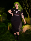 Full length shot of model wearing the BEETLEJUICE™ Lydia Dead Tee over a long black skirt and paired with black combat boots to finish the look.