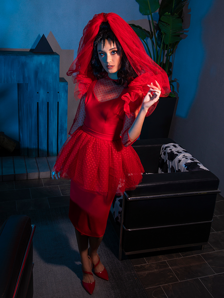 Full length shot of BEETLEJUICE™ Lydia Dress pulling aside the red veil she's wearing that matches her entire outfit.