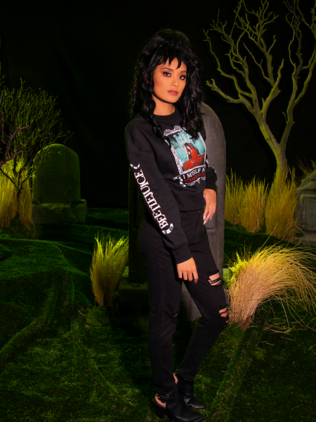 Full length shot of female model with black hair standing in a spooky cemetery and wearing the BEETLEJUICE™ Lydia Strange Long Sleeve Tee.