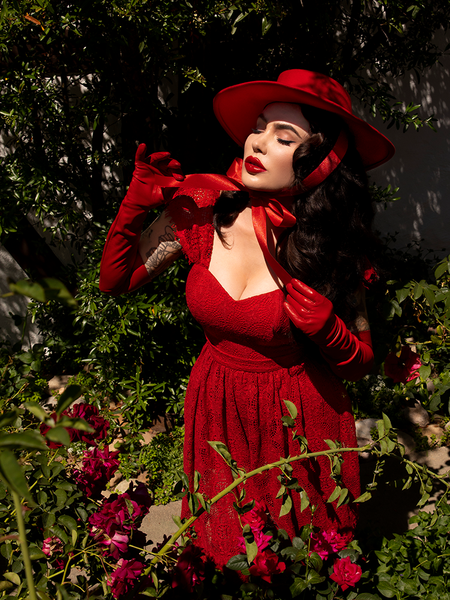 Micheline Pitt leaning forward to show off the ribbon on the Faux Leather Opera Gloves in Crimson from goth clothing company La Femme en Noir.