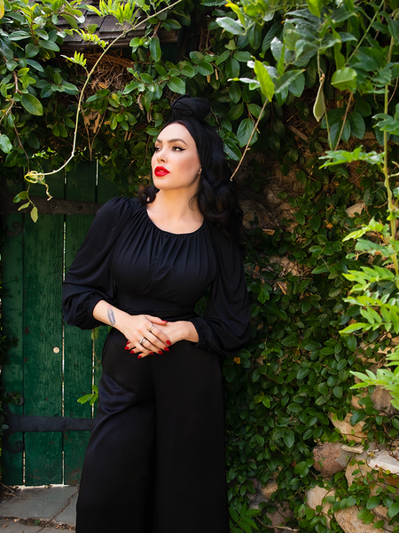 Micheline Pitt posing with her hands resting at her midsection and looking off to the camera in her gothic vintage clothing.