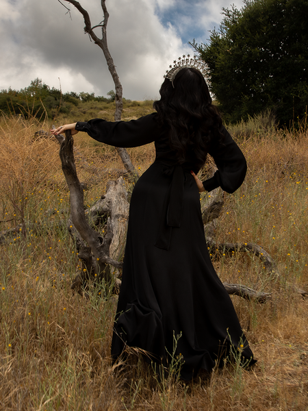 Looking away from the camera and up at grey skies, Micheline Pitt gives us a look at the back of the Opera Satin Gown in Black.