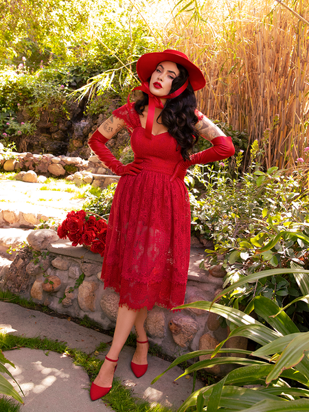 Micheline Pitt standing with her hands on her hips and looking directly at the camera wearing an all crimson gothic retro outfit.