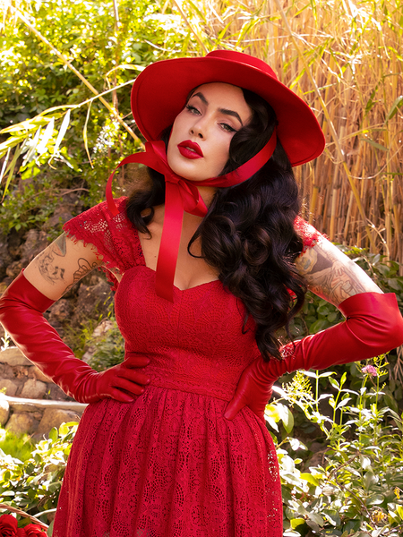 With her hands on her hips, Micheline Pitt looks into the camera while wearing an all crimson red gothic retro clothing outfit.