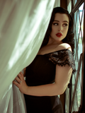 Rachel leans on a window and pulls back a white curtain while modeling the Southern Gothic bustier top in black.