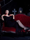 Laying back on a red velvet couch, Heather Black models the Vampira® Show Gown from goth fashion clothing brand La Femme en Noir.