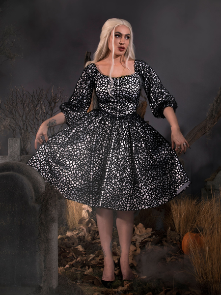 Looking off camera while standing in a cemetery, Micheline models the gothic Sleepy Hollow™ Lady Van Tassel Guipire Lace Dress by La Femme En Noir.