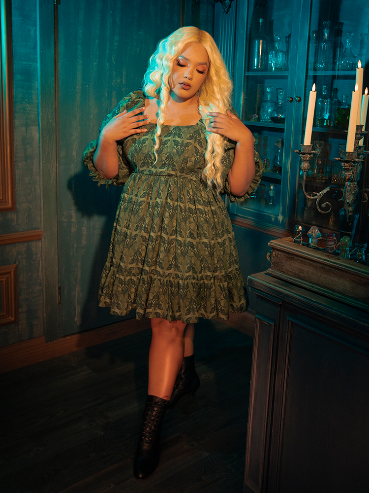 Embrace the dark allure of the CRIMSON PEAK™ Allerdale Moth Wallpaper Babydoll Dress. The olive backdrop, rich and earthy, sets the stage for a dance of moths — creatures of the night drawn to the unseen and the unknown. This dress embodies the delicate balance between darkness and light, offering a unique statement piece for those who walk the path less traveled.