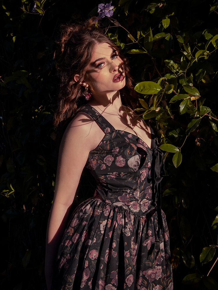 Bathed in twilight, the auburn-haired muse embodies ethereal grace in the Ambrosia Dress, its Decayed Beauty print whispering tales of withered roses and moonlit gardens.