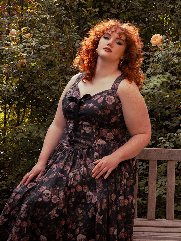 The auburn glow of her hair ignites the dusky palette of the dress, a harmony of fire and decay against the darkness.