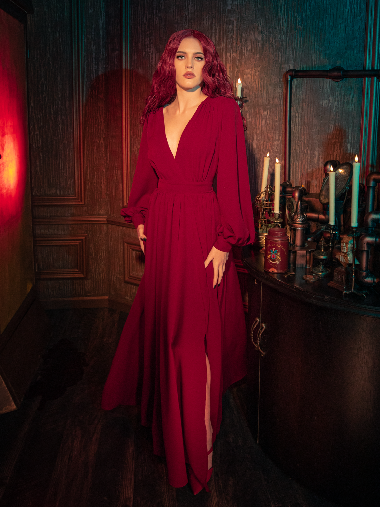 A model poses in the crimson red Belladonna gown, highlighting the off-center front slit and the dramatic sweep of the skirt, perfect for a Whimsigoth or dark cottagecore aesthetic.