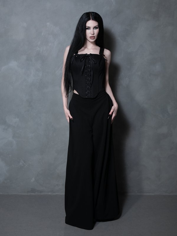 A female model stands as an icon of gothic glamour, wearing a structured black cotton corset imbued with dark elegance.