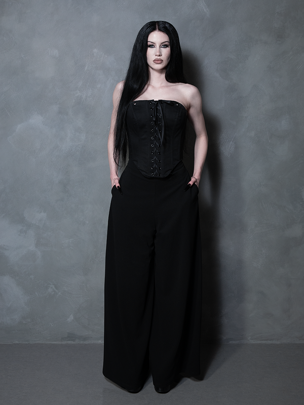 Evoking a hauntingly beautiful Victorian goth atmosphere, a female model wears an structured black textile corset.